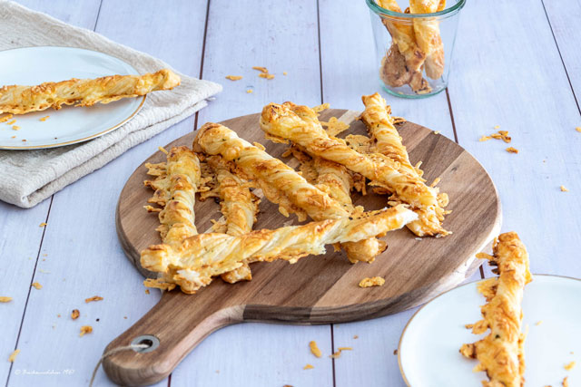 knusprige Blätterteig-Käsestangen mit Kräuterbutter und goldbraunen Käse auf einem Holzbrett