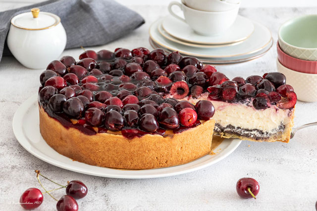 Frischer Kirsch-Mohn-Käsekuchen mit cremiger Quarkfüllung, Mohnschicht und frischen Kirschen auf einer Kuchenplatte